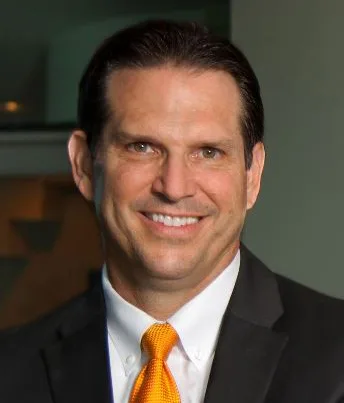 Walter, satisfied customer in black suit and orange tie, giving testimonial about 25 years of bespoke tailoring success with Beth Raymond at From Collars to Cuffs in Weston, South Florida