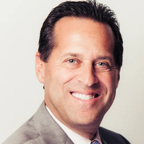 Satisfied client Steve smiling in a suit, sharing a testimonial about 20 years of wearing Beth Raymond's high-quality custom shirts at From Collars to Cuffs in Weston, South Florida