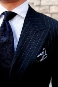 Close-up of a man wearing a custom navy pinstripe suit with a dark textured tie and white pocket square, highlighting luxury formal menswear and tailoring craftsmanship at From Collars to Cuffs in Weston, Florida