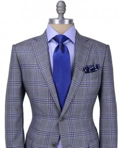 Tailor's mannequin wearing a custom grey plaid suit jacket, light blue shirt, solid blue tie, and patterned pocket square, representing premium bespoke menswear styling at From Collars to Cuffs in Weston, Florida