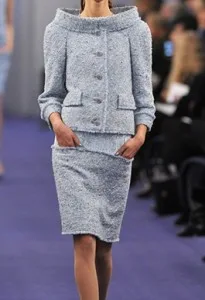 Model on a runway wearing a custom light blue tweed suit with a boat neck jacket and matching skirt, highlighting luxury bespoke tailoring and premium fabric selection at From Collars to Cuffs.