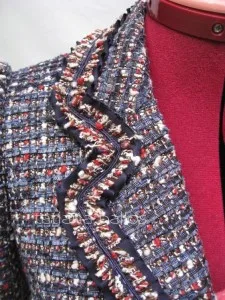 Detailed view of a custom tweed jacket featuring navy piping, red buttons, and premium bouclé fabric texture, showcasing expert tailoring details at From Collars to Cuffs in Weston, Florida