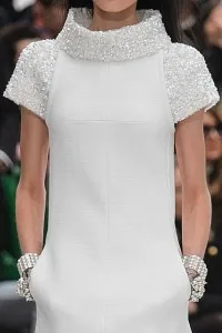 Woman in a custom white dress featuring a heavily embellished pearl high neck and short sleeves, representing elegant bespoke evening gowns crafted at From Collars to Cuffs in Weston, Florida