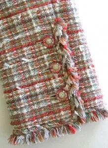 Detailed view of a custom multi-colored tweed fabric with red, green, and white threads and frayed fringe trim, representing luxury bouclé materials available at From Collars to Cuffs in South Florida