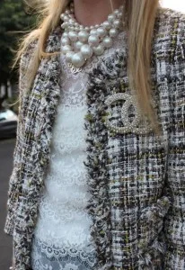 Woman wearing a custom multi-colored tweed jacket layered over a white lace top with a large pearl necklace and Chanel brooch, showcasing high-end bespoke styling at From Collars to Cuffs in Florida