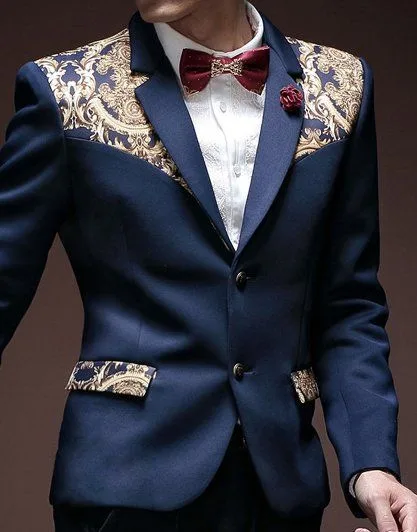 Model in a custom navy tuxedo featuring ornate gold baroque embroidery on the shoulders and pockets with a burgundy bow tie, showcasing luxury bespoke formal fashion at From Collars to Cuffs in Weston, Florida.