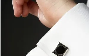 Close-up of a custom white dress shirt cuff featuring a sleek black square cufflink, representing luxury menswear accessories and personalized detailing at From Collars to Cuffs in Florida