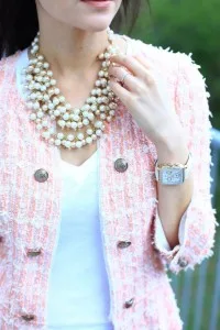 Close-up of a woman wearing a custom pink tweed jacket with frayed edges and a large pearl necklace, showcasing high-end bespoke women's fashion and accessories from From Collars to Cuffs.