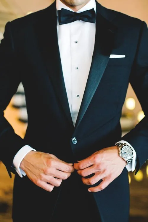 Man adjusting his custom black tuxedo jacket over a dress shirt and bow tie, demonstrating precise fit and craftsmanship for black tie attire at From Collars to Cuffs in Weston, FL