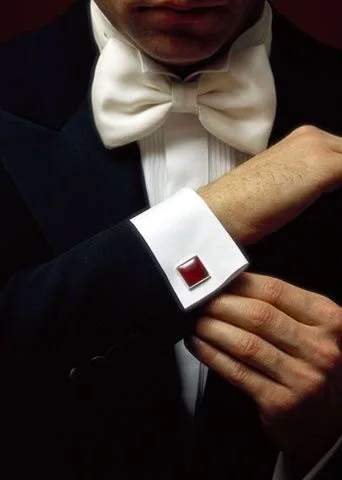Close-up of a man adjusting red cufflinks on white French cuffs with a white bow tie, showcasing luxury bespoke formal wear accessories at From Collars to Cuffs in Weston, Florida.