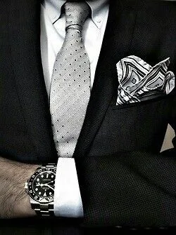 Close-up of a man in a custom black suit with a silver patterned tie, decorative pocket square, and luxury watch, highlighting sophisticated men's formal wear at From Collars to Cuffs in South Florida.