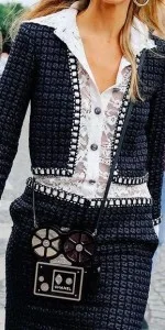 Model in a custom navy tweed jacket and skirt with white piping and a camera bag, highlighting elegant bespoke women's suits at From Collars to Cuffs in South Florida