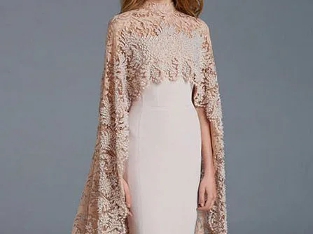 Woman in a custom light peach dress with delicate lace cape sleeves, showcasing romantic bespoke evening fashion and intricate lace detailing at From Collars to Cuffs in Weston, Florida.
