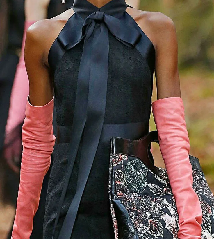 Model wearing a custom black halter dress with a dramatic bow detail at the neck paired with pink opera gloves, showcasing elegant bespoke fashion styling at From Collars to Cuffs in Weston, Florida.