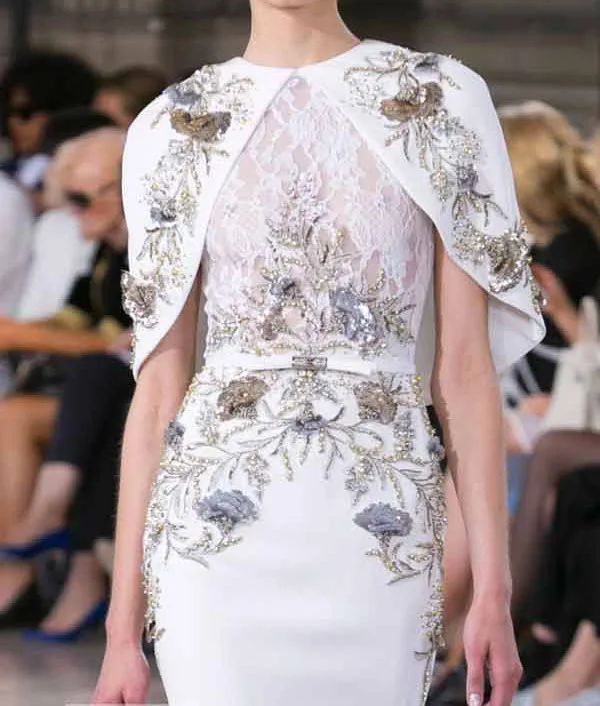 Woman in a custom white dress featuring intricate gold and silver floral embroidery on the bodice and cape sleeves, representing haute couture bespoke fashion at From Collars to Cuffs in Weston, Florida.