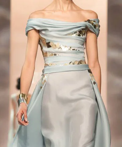 Model wearing a custom light blue silk off-the-shoulder gown with a draped neckline and metallic belt detail, representing elegant bespoke formal wear at From Collars to Cuffs in Weston, Florida.