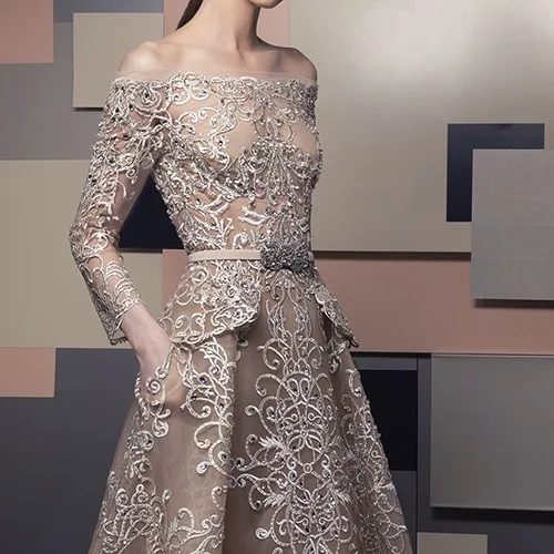 Model wearing a custom off-the-shoulder sheer evening gown with intricate silver embroidery and long sleeves, showcasing bespoke luxury formal wear at From Collars to Cuffs in South Florida