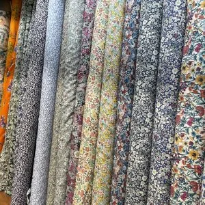 Selection of rolled cotton fabrics featuring small ditsy floral patterns in blue, white, and yellow, representing high-quality fabric choices for custom shirting and dresses at From Collars to Cuffs in South Florida.