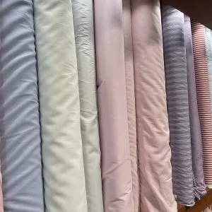 Selection of high-quality fabric rolls in solid pastels, blues, and subtle stripes, representing premium cotton and linen materials for bespoke shirts and pants at From Collars to Cuffs in South Florida.
