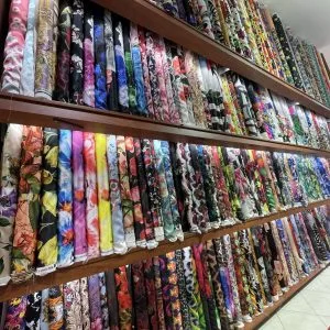 Walls of fabric bolts featuring vibrant floral and designer prints, showcasing the massive selection of luxury textiles for custom fashion at From Collars to Cuffs in Weston, Florida.