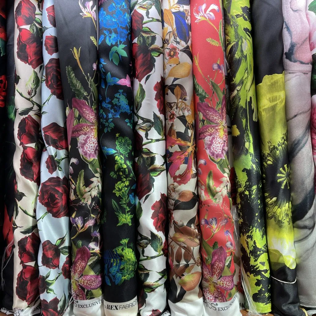 Display of hanging fabric bolts featuring vibrant floral prints, tropical patterns, and bold colors, highlighting the diverse silk and textile options for custom fashion at From Collars to Cuffs in South Florida.
