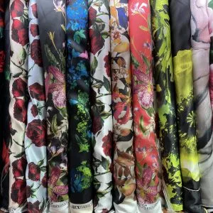 Display of hanging fabric bolts featuring vibrant floral prints, tropical patterns, and bold colors, highlighting the diverse silk and textile options for custom fashion at From Collars to Cuffs in South Florida.