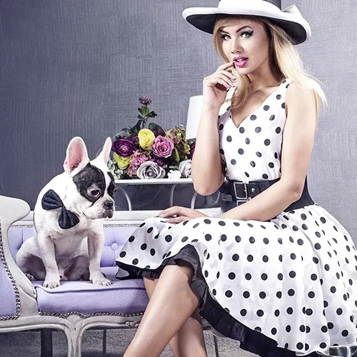 Elegant woman wearing custom white polka dot Chanel-inspired dress with black belt and wide-brim hat, sitting with French bulldog at From Collars to Cuffs boutique in Weston, South Florida