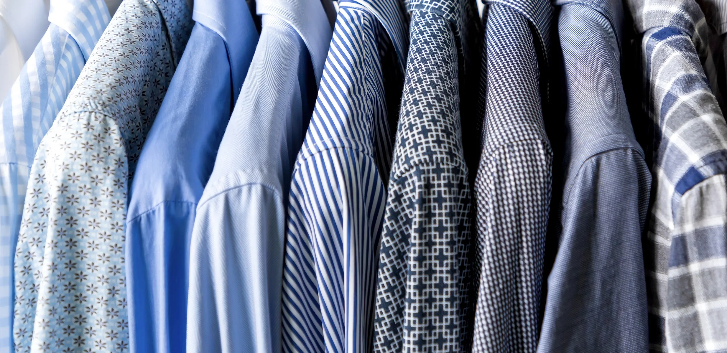 Row of premium custom dress shirts displaying exclusive fabrics like stripes, geometric patterns, and solid blues for bespoke tailoring at From Collars to Cuffs in Weston, Florida