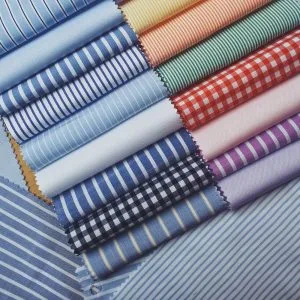 Collection of folded fabric swatches showing various stripes, checks, and solid colors, showcasing the extensive material options for custom shirts available at From Collars to Cuffs in South Florida.