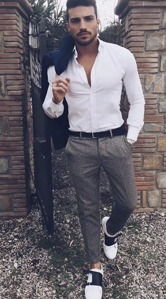Man in a custom white dress shirt and grey tailored pants holding a sport jacket, representing luxury European fabrics from Zegna, Loro Piana, and Armani for bespoke menswear at From Collars to Cuffs in Weston, Florida