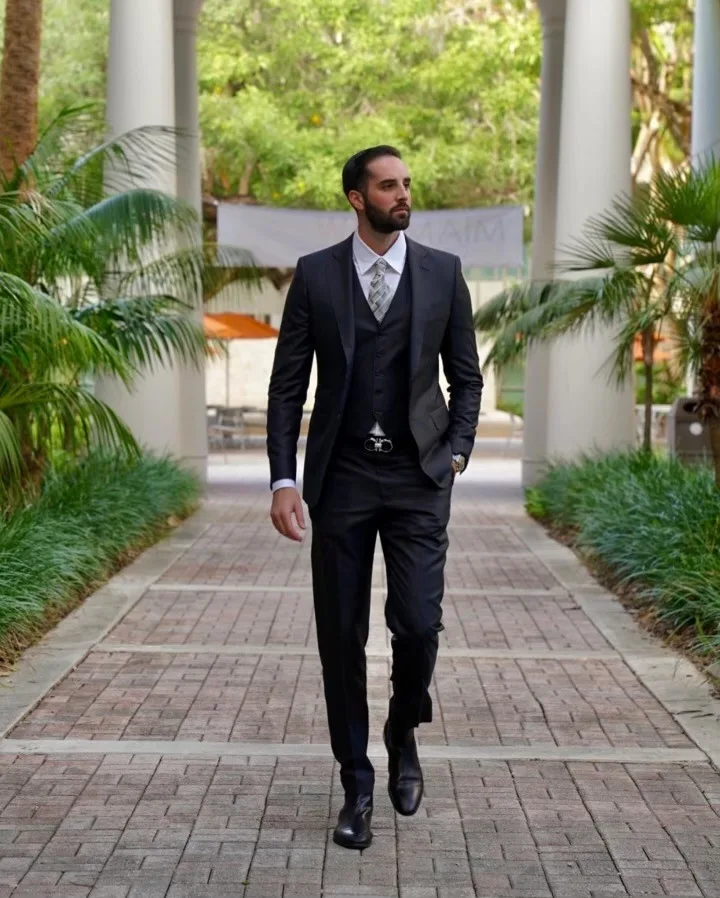 Man walking confidently in a custom black 3-piece suit, showcasing impeccable fit and bespoke tailoring at From Collars to Cuffs in Weston, FL