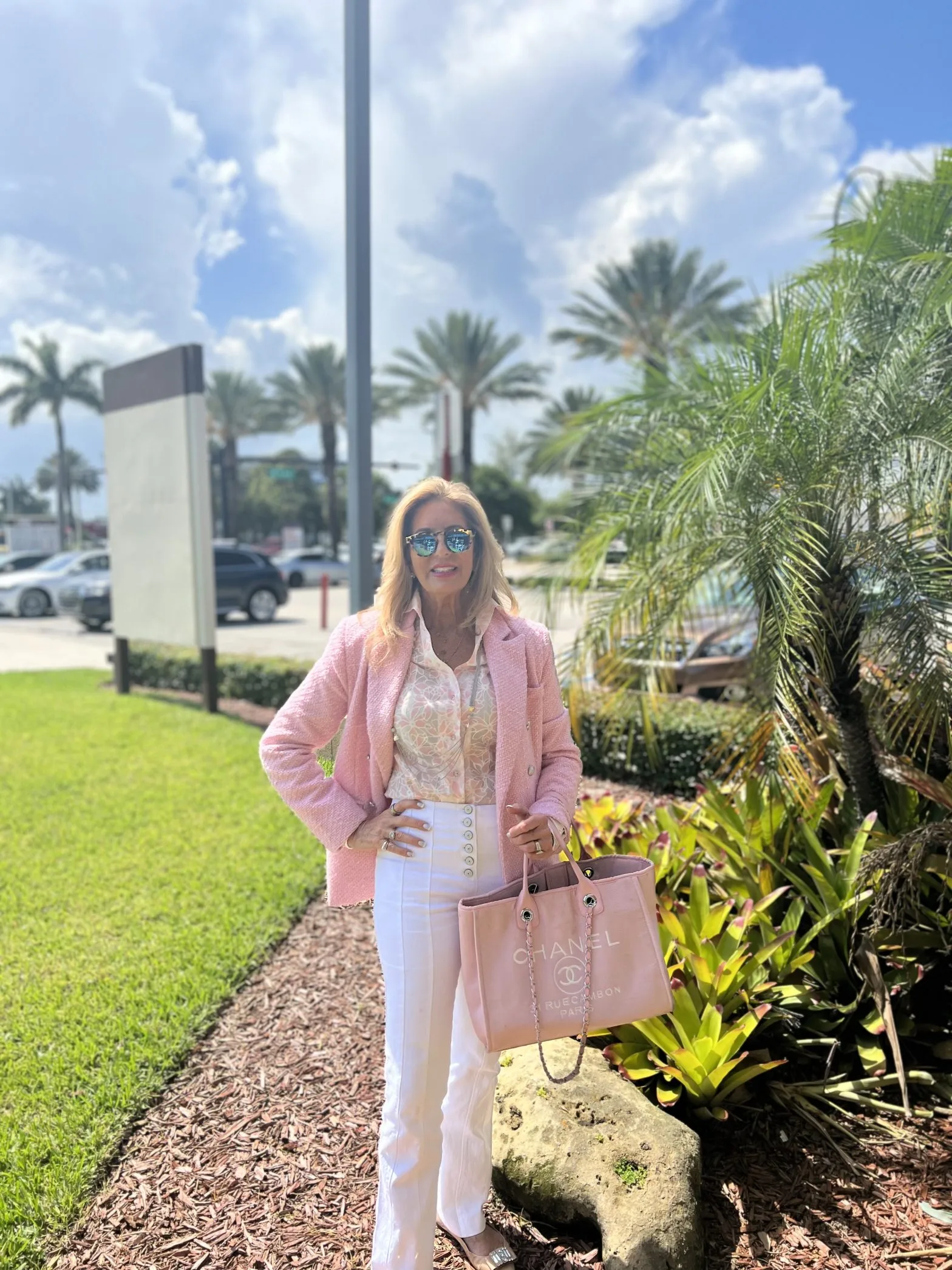 Woman wearing a custom pink bouclé jacket with white high-waisted pants and Chanel bag, showcasing casual Florida resort wear and bespoke tailoring at From Collars to Cuffs in Weston, South Florida